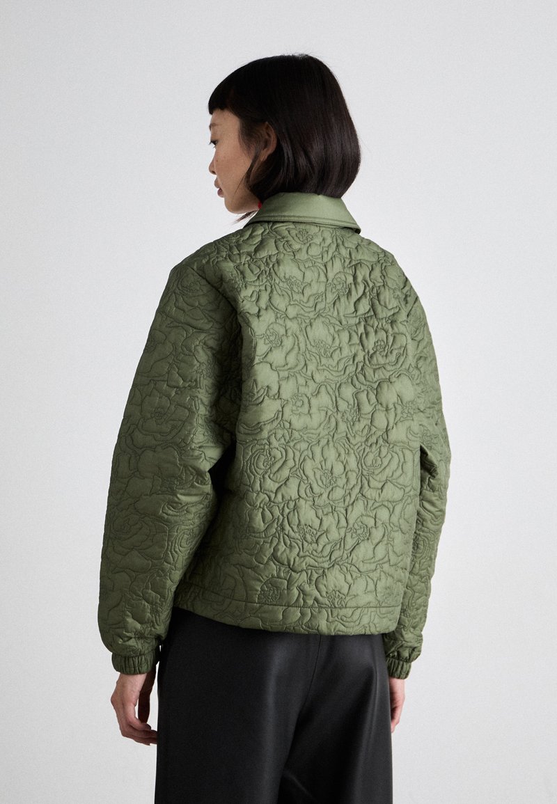 Grüne gesteppte Jacke mit einem floral eingeprägten Muster, einem Kragen und gerippten Bündchen. Das Design ist locker sitzend und hat eine kürzere Länge.