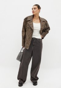 Giubbotto in ecopelle marrone con ampi revers, abbinato a una maglietta bianca a coste e jeans neri a gamba larga. Gli accessori includono una borsa grigia.