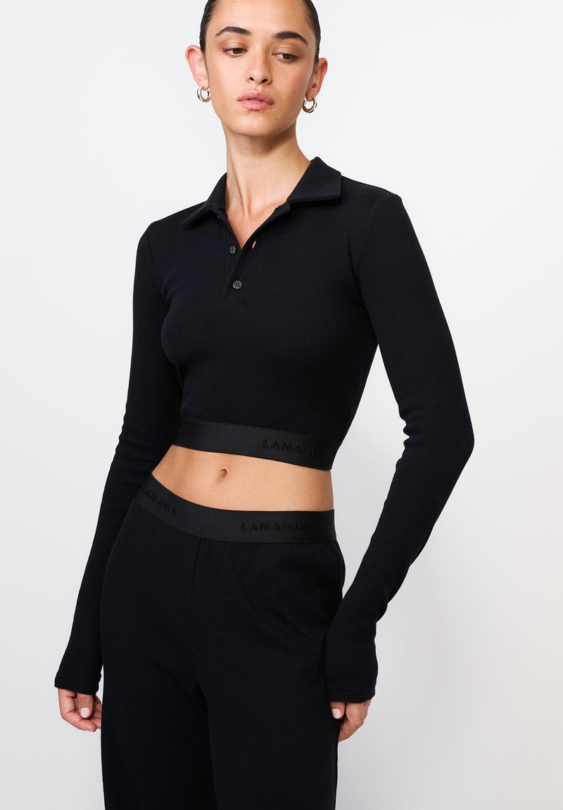 Fekete bordázott hosszúujjú crop top gombos nyakkal és tónusos rugalmas derékkal, amelyen a "LAMANIA" logó található.