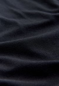 Black fabric with a soft, smooth texture, displaying gentle folds and creases. The material appears lightweight and stretchy.