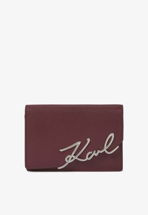 Burgundy leather wallet with a smooth texture, featuring a prominent silver "Karl" logo as a clasp. Compact rectangular design.