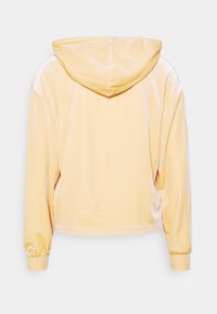 Sweat à capuche en velours jaune pâle doux avec manches longues et poignets élastiques, vu de dos sur un fond uni.