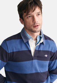 Polo a maniche lunghe a righe blu e navy con colletto e patta dei bottoni bianca. Tessuto in cotone morbido con un logo distintivo.