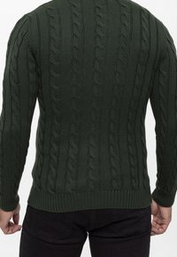 Gebreide trui in donker groen met een textuur van kabelpatroon, geribbelde manchetten en zoom. Gemaakt van een dikke, warme stof.