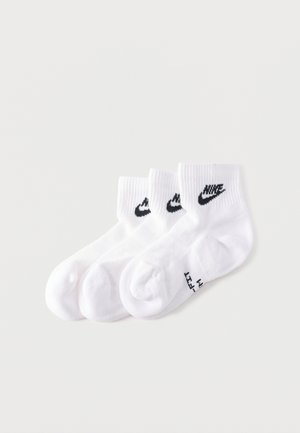 Trzy pary białych skarpetek do kostki z czarnymi logo Nike Swoosh ułożone obok siebie na białym tle.