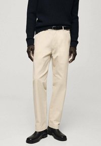 Beige chino kalhoty vyrobené z bavlny se střih přímého nohavice, s bočními kapsami a zipem. Kombinované s námořnickým žebrovaným svetr a černými botami.