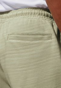 Világoszöld, bordás anyagú joggers, elasztikus derékkal és egy hátizsebbel. A textúra enyhén texturált és puha.