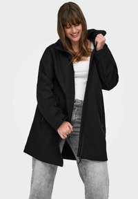 Chaqueta negra con capucha, cierre frontal y bolsillos laterales. Tiene una textura suave y un ajuste relajado, ligeramente oversize.