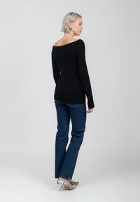 Maglione nero off-shoulder con maniche lunghe e silhouette aderente. Abbinato a jeans blu a gamba dritta e scarpe con tacco a stampa serpente.
