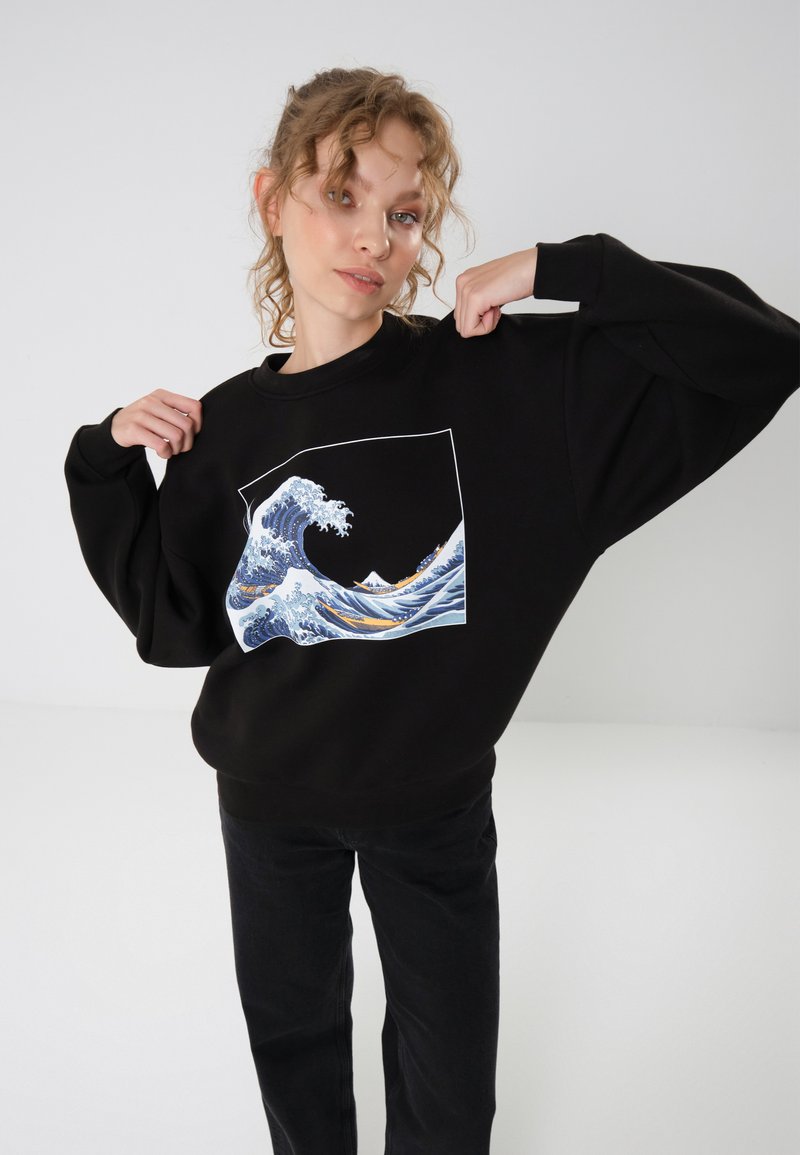 Black sweatshirt with a large wave graphic in blue and white. Features a relaxed fit and ribbed cuffs. Worn with black pants.