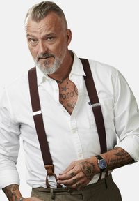 Rudos petnešos su odiniais akcentais nešiojami virš baltos marškinių su mygtukais; matomi tatuiruotės ir juodas laikrodis užbaigia aprangą.