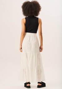 White, tiered maxi skirt with eyelet pattern and elastic waistband, paired with a black ribbed sleeveless top and black sandals.