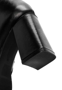 Zapato de cuero negro con tacón, que presenta un tacón cuadrado con un acabado suave y brillante y una punta redondeada. La suela tiene textura para un mejor agarre.