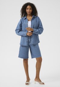 Denim komplekt, mis sisaldab triibulist nööpidega särk ja sobivaid lühikesi pükse. Kangas on helesinine vertikaalsete valgete triipudega.