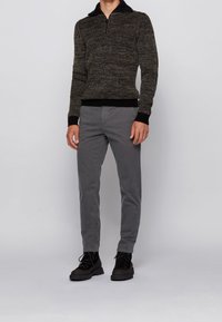 Stickad svart och guldfärgad tröja med hög krage, kombinerad med grå chinos och svarta snörskor. Mjuk textur, figursydd design.