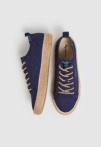 Námořnické plátěné tenisky s tkaným jutu podobným béžovým podpatkem, kulatou špičkou, kontrastními otvory na šňůrky a značkou na stélce.