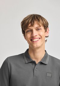 Grå pikétröja med ett texturerat tyg, två grå ränder på kragen och en fyrkantig logotypremsa på vänster bröst.