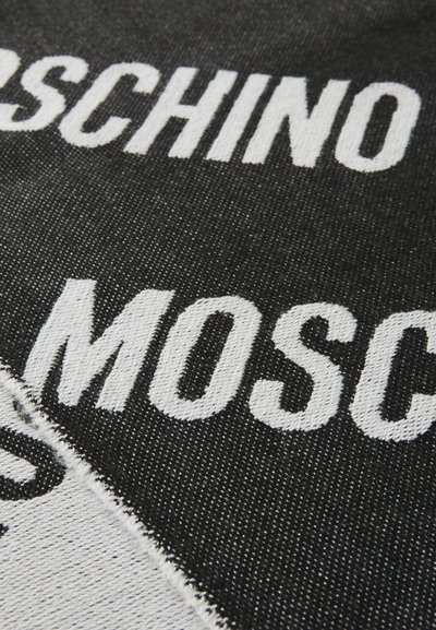 Musta kangas, jossa on rohkeaa valkoista tekstiä "MOSCHINO" ja "MILANO". Materiaalissa on teksturoitu kudonta ja näkyviä ompelutekstuuritietoja.