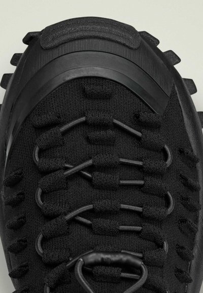 Scarpa sportiva nera con upper testurizzato, sistema di allacciatura elastica e suola robusta. Accenti in gomma notevoli e design elegante e aerodinamico.