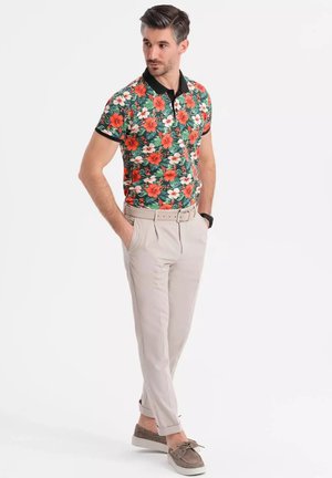Blomstret polo-shirt i grøn med røde og hvide blomster, parret med lyse beige bukser. Har en sort krave og oprullede ærmer.