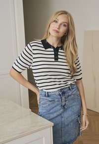 Gestreiftes kurzärmliges Poloshirt in Weiß und Schwarz, mit einem schwarzen Kragen und einer Drei-Knopf-Leiste; kombiniert mit einem Jeans-Bleistiftrock.