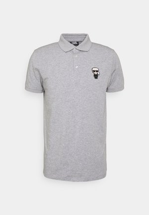 Polo de manga corta de color gris claro con cuello y dos botones, con un pequeño logo de dibujos animados en blanco y negro en el pecho izquierdo.