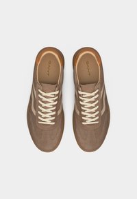 Ζευγάρι καφέ σουέτ αθλητικά παπούτσια με μπεζ ρίγες, λευκά κορδόνια και ανοιχτά καφέ διακοσμητικά, σε θέα από πάνω σε λευκό φόντο.