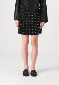 Svart mini skjørt med metalliske nagler, glatt tekstur og en tettsittende form. Kombinert med svarte slip-on loafers.