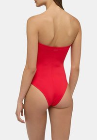 Costume da bagno intero rosso con design senza spalline, tessuto liscio e schiena bassa. Presenta un branding sottile sul retro.
