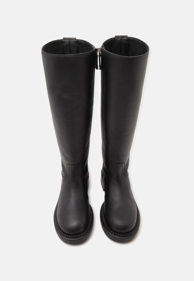 Paire de bottes hautes en cuir noir avec bouts arrondis et fermetures éclair latérales visibles, présentées debout sur un fond blanc uni.