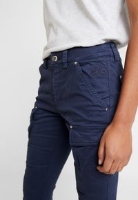 Granatowe spodnie cargo z fakturowanym wykończeniem, z bocznymi kieszeniami, zapięciem na guziki oraz dyskretnym haftowanym logo z przodu.