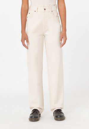 Pantalones de mezclilla de pierna ancha en color beige, con una cintura alta, cierre de botón metálico y bolsillos laterales, combinados con unos zapatos negros.