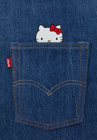 Personnage Hello Kitty avec un nœud rouge dépassant du haut de la poche arrière en denim bleu Levi's avec des coutures orange.