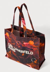 Πανέμορφη επαναχρησιμοποιήσιμη τσάντα αγορών με πολύχρωμο αφηρημένο σχέδιο σε αποχρώσεις κόκκινου και μαύρου, διαθέτει διπλούς υφασμάτινους ιμάντες και λευκό λογότυπο της μάρκας.