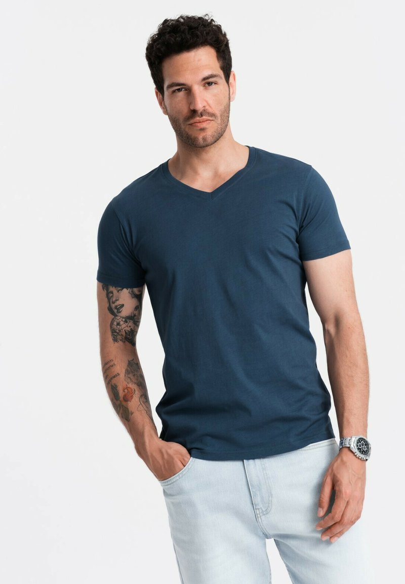 Námořnická modrá v-neck tričko vyrobené z měkké látky, spárované s světle modrými džíny. Má krátké rukávy a pohodlný střih.