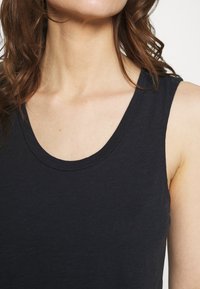 Canotta nera senza maniche con scollo rotondo, texture liscia e dettagli di cucitura minimi. Il tessuto appare morbido e leggermente elasticizzato.