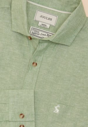 Heled roheline linase segu särk, millel on nööbiga krae, ees tasku ja väike valge logo. Pruunid nööbid kinnitamiseks.