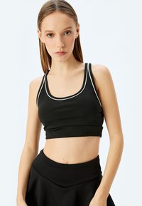 Sort atletisk crop top med hvid piping, der har en scoop-udskæring og smalle skulderstropper. Glat, strækbart materiale; tætsiddende design.