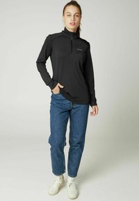 Schwarzer Pullover mit langen Ärmeln und Zip-Kragen, aus leichtem Material, kombiniert mit hoch geschnittenen blauen Jeans und weißen Turnschuhen.
