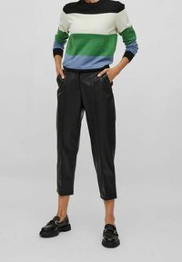 Raidallinen neule vihreässä, sinisessä, kermanvärisessä ja mustassa; istuvat mustat keinonahkahousut; kiiltävät mustat loaferit, joissa on kullanväriset koristeet.