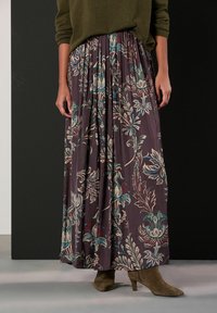 Maxisukně s plisováním tmavě fialové barvy s květinovými vzory v krémové, modrozelené a bordó. Kombinováno s hnědými botami na podpatku pro kontrast.