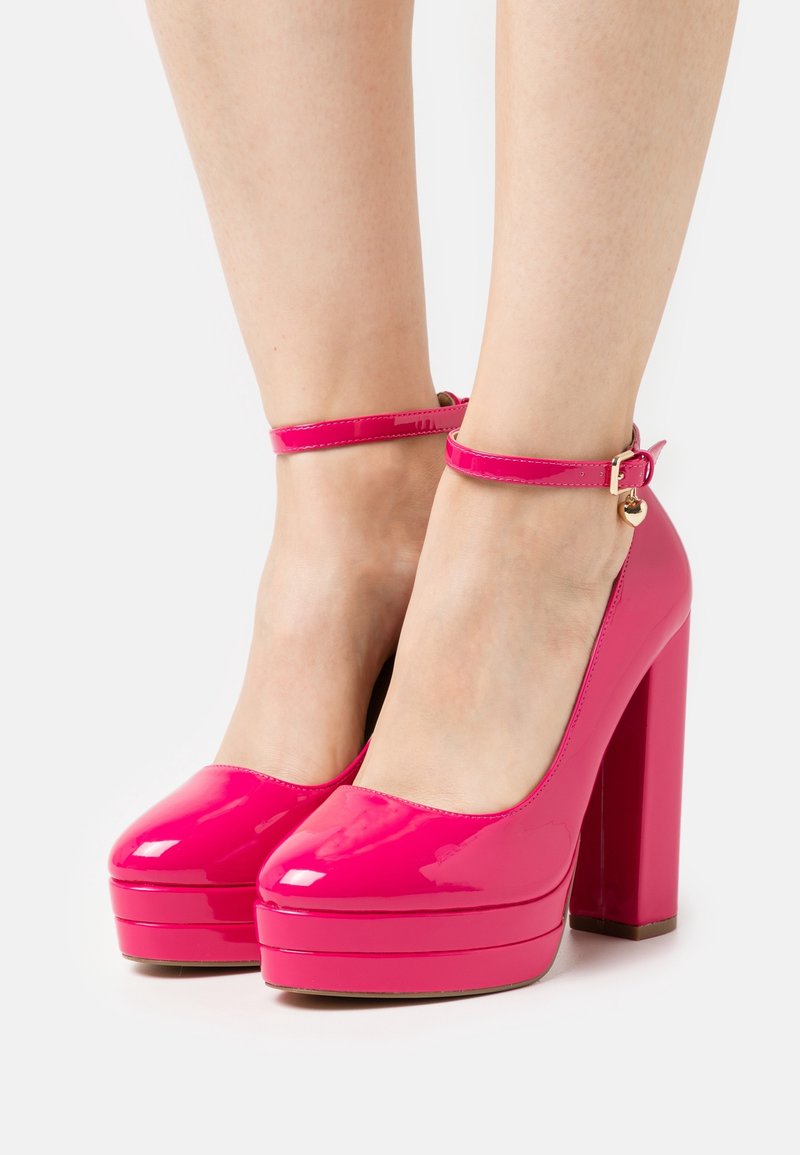 Escarpins compensés en cuir verni rose vif avec un bout arrondi, une bride à la cheville et un talon bloc haut, présentant une finition brillante.