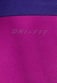 Violetti ja fukssin värinen Dri-FIT-kangas, jossa on sileä rakenne, neulekuvio ja saumaton siirtymä värilohkojen välillä.