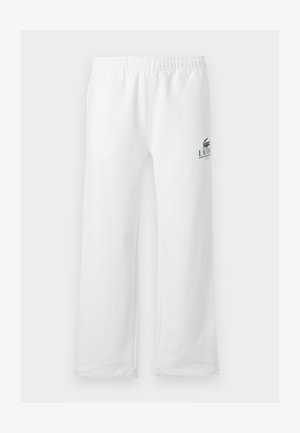 Deux personnes se tiennent côte à côte, portant des chemises vertes Lacoste et des pantalons blancs Lacoste, sur un fond blanc uni.