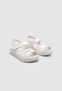 Sandalias blancas con un tacón bajo en forma de cuña, que presentan correas anchas, un diseño de punta abierta y una textura suave parecida al cuero.