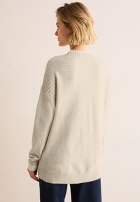 Hellgrauer gestrickter Pullover mit Rippdetails an Schultern und Bündchen, lockerer Schnitt, leicht längerer Rücken, weicher Textur.