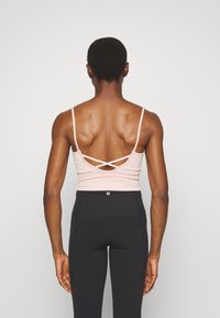 Top justo cor-de-rosa claro com alças finas, apresentando um design de costas cruzadas. Combinado com leggings atléticas pretas de cintura alta.