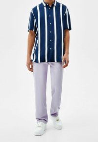 Kortärmad skjorta i marinblått med vita vertikala ränder, kombinerad med ljuslavendelfärgade byxor och vita sneakers. Bomullsblandat tyg.