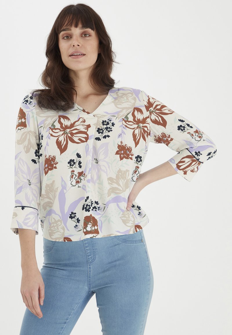 Blusa floreale color crema, con motivi marroni, lavanda e blu scuro. Tessuto morbido con scollatura a V e maniche a 3/4, vestibilità morbida.