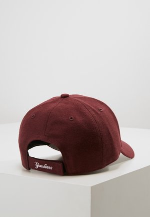 Gorra de béisbol granate con correa ajustable, texto bordado "Yankees" en la parte trasera, colocada sobre una superficie blanca con un fondo liso.